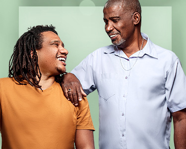 Pai e filho se olhando e sorrindo em um momento de afeto, eles usam camisas básicas e joias masculinas
