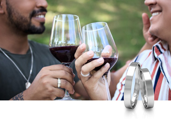 Casal bebendo vinho em um parque, eles usam alianças de compromisso no dedo anelar
