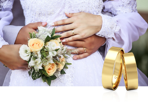 Noivos abraçados em foto do pós-wedding, eles usam alianças de casamento tradicionais em ouro 18K e ela segura o buquê