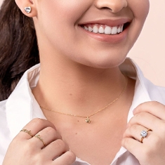 Mulher sorrindo usando anéis de ouro e um colar de ouro em formato de coração