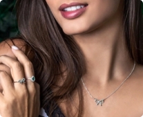 Mulher usando um mix de joias, com colar de lacinho e dois anéis de prata