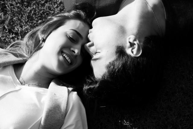 Homem e mulher deitados em um gramado, o namorado beija a testa da companheira