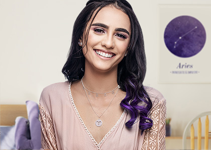 Menina usando uma choker com estrelas e um colar com o símbolo do signo. Ao fundo, um quadro de áries.