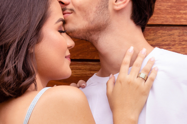 Comprar alianças de namoro Casal abraçado com o homem beijando a testa da sua parceira. A mulher possui uma aliança de compromisso em sua mão.