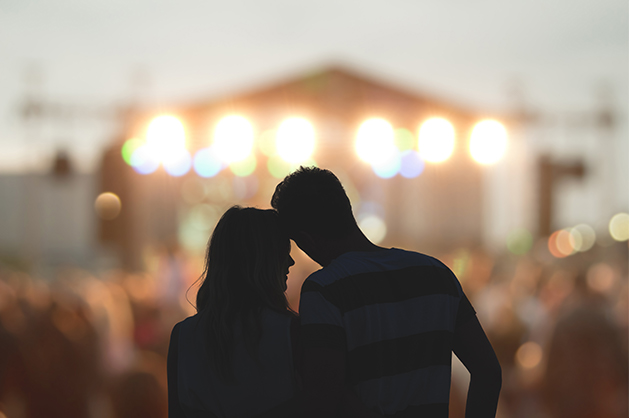 Silhueta de um casal assistindo show com luzes e o palco em segundo plano