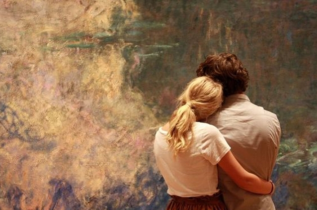 Casal abraçados observam um uqadro em um museu