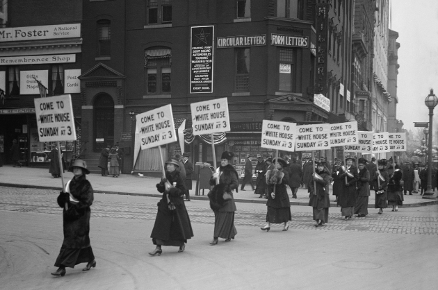 Imagem antiga em preto e branco de mulheres marchando em manifestação carregando placas