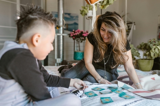 Mãe e filho riem jogando cartas em cima de uma cama