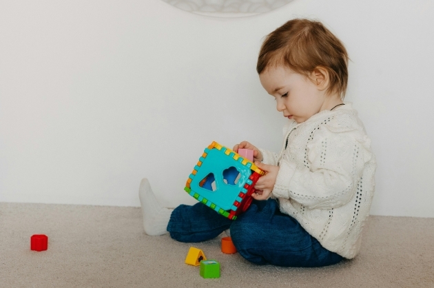 Bebê brinca com caixa de encaixar peças coloridas sentada no chão