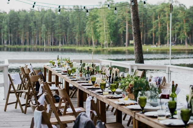 Mesa de convidados para casamento rústico à beira de um lago, a mesa e as cadeiras são de madeira