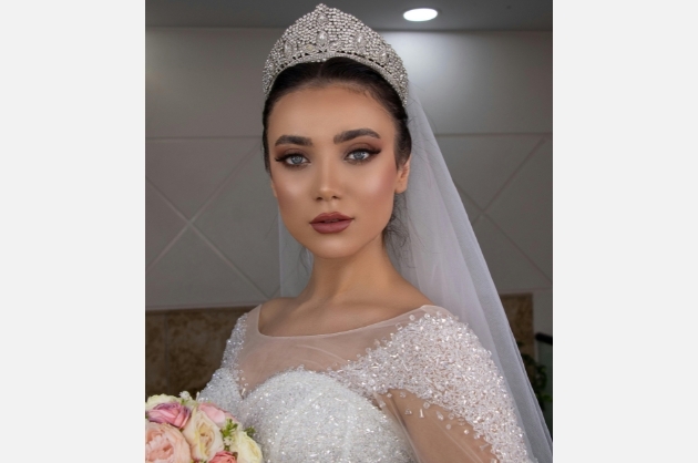 Noiva encara a câmera usando véu e grinalda e segurando um buquê de rosas amarelas e rosas
