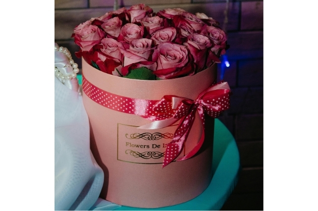 Caixa redonda cor de rosa repleta com rosas e laço de fita