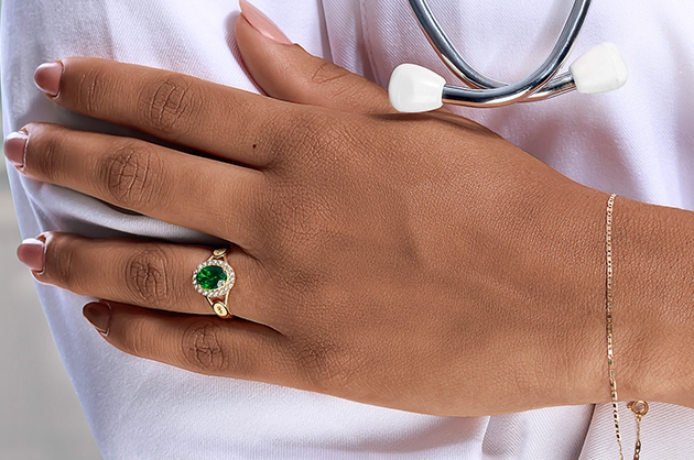 Imagem de mão de uma mulher com roupa de médica com anel de formatura com pedra verde